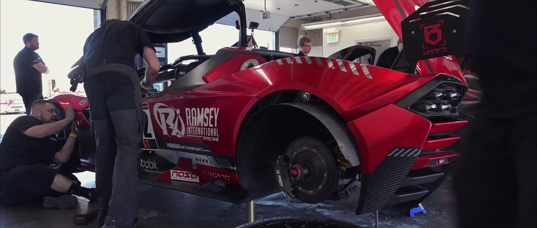 The race car up on stands in the garage with the crew working around it